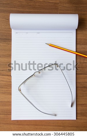 Notebook, pencil and eye glasses on wood background