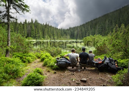 Three person are sitting on a bench by the lake