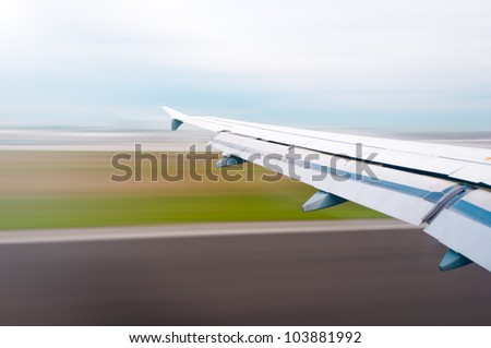 View of air plane wing during take off or landing. Motion blur of airport grounds and sky.
