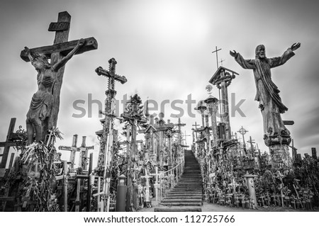 Hill of crosses in Siauliai, the city of Lithuania. Old stairway goes to gray sky. Stairs lead to the top of hill. Crosses and statues of saints near. Sun shines weakly, so place looks mysterious.