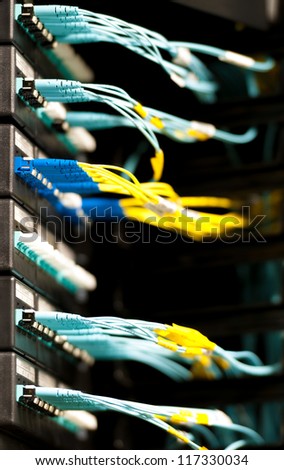 Internet service provider equipment. Focus on panel with optic cables connected to panel in datacenter. Network server room. Modern technology. Yellow and blue cables contrast with dark background.