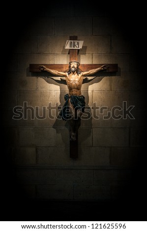 Crucifix on wall in spotlight inside old dark church or cathedral. Jesus Christ on cross. Religion, belief and hope. Holy and sacred places.