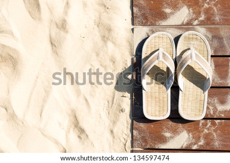 Sand and beige flip flops. Pair of sandals on boardwalk. Walk on sand in bright sunny day, Leisure time at beach. Creative concept of carefree vacations. Popular outdoor activity in summer.