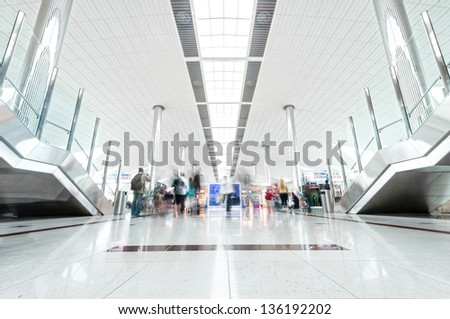 Big light hall in Dubai airport with passengers in hurry. United Arab Emirates. Modern style interior with shining metal constructions and lot of light. Travelling and tourism.