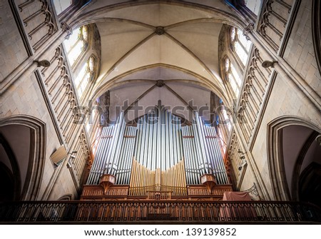 Great pipe organ under arched ceiling in old catholic church shining in sunlight. View from below. Largest musical instrument mostly used in church service in western countries.
