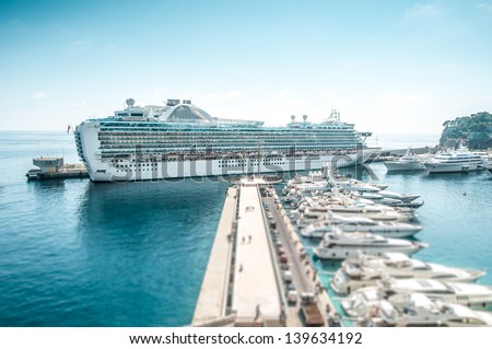 Large cruise ship in port. Luxury liner in blue water under clear sky with lots of yachts on berth in foreground. Comfortable cruise or voyage. Travelling and tourism on summer holidays and vacations.