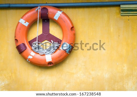 Yellow wall with orange buoy on it. Old lifebuoy with rope inside. Equipment for rescue of people. Precaution for survival in sea. Painted surface with pipe and ring-buoy. Service for lifesaving.