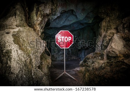 Entry to dangerous cave blocked with red and white Stop sign. Warning about danger on way to dark cave. Prohibitive sign at entrance to grot. Risky tourism and travelling.