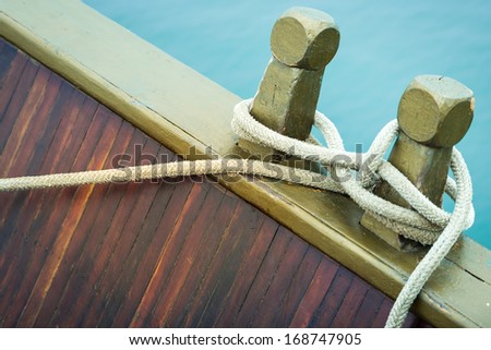 Marine rope tied into knot in foreground, white background. Close-up of nautical equipment for mooring. Focus on detail of ship. Twisted rope wrapped around. Sea travel.