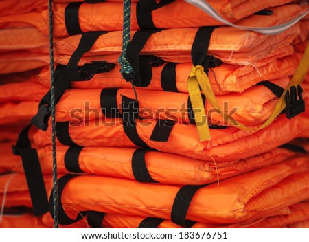 Close-up view of packed orange life-jackets pile ready for shipping. String with hook holding jacket. Safety control on board ship. Sea travelling.