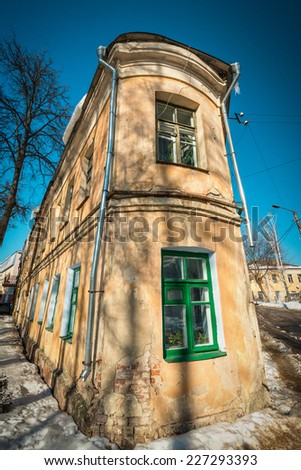 Old building exterior view, requiring repair. Dirty-orange color building. Multiple windows with green frames. Flower pots in windows. Bright cloudless winter day. Kaluga, Russia.