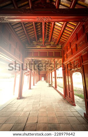 Beautiful red wooden hall with golden ornate details in Hue citadel, Vietnam, Asia. Vanishing roof and tiled floor. Sunlight through columns. Famous destination for tourists. UNESCO Heritage site.