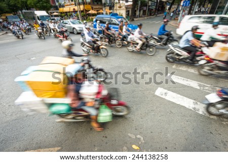 Motion view of street in Vietnam. Southeast Asia. Busy daily traffic with stream of motorbikes and cars. Blurry view of weighted scooter in foreground. Transportation and traffic.
