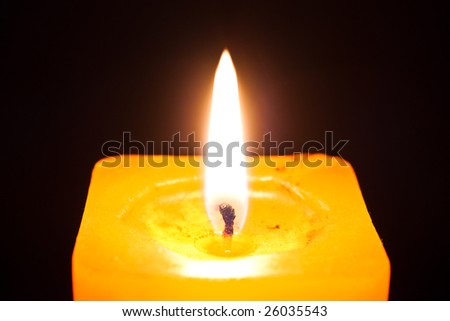 close up photo of the yellow burning candle isolated on black background