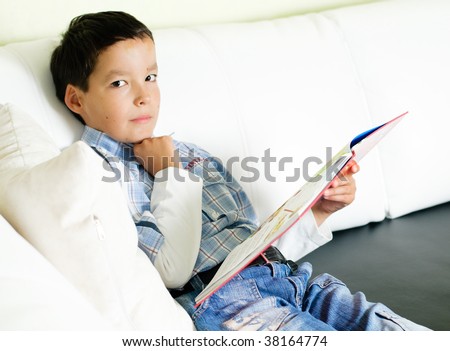 thoughtful little boy sitting on a sofa and reading a book