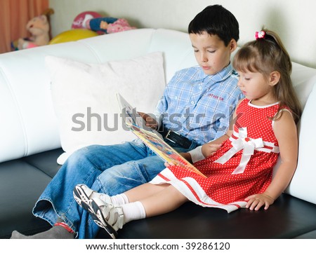 little boy sitting on a sofa and reading a book to his sister