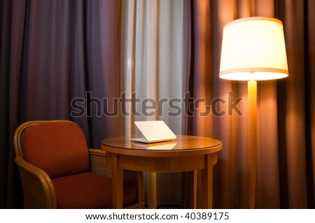 notebook computer on the table in the room with lamp, chair and curtains on the window