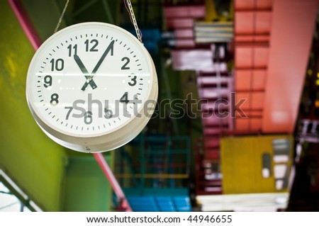 big clock hanging down from factory ceiling