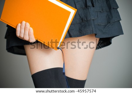 view of the lower body part of woman wearing skirt and stockings holding book in her hands