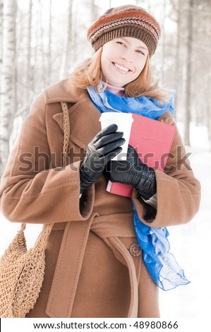 winter street portrait of young beautiful natural looking woman in casual clothes holding books, drinking coffee and smiling