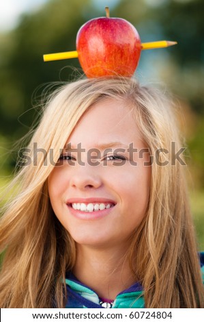 beautiful young student girl standing in park, smiling and looking into the camera, with red apple on her head