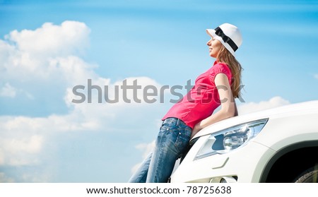 Beautiful young woman resting at bonnet of her car with her eyes closed and blue cloudy sky in background