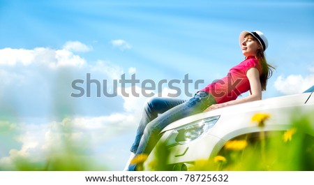Beautiful young woman resting at bonnet of her car at flower field with blue cloudy sky in background