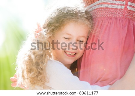 beautiful little and happy daughter hugging her mother. Nature background.