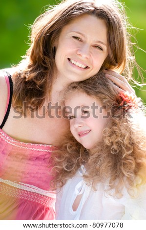 Beautiful and happy young mother on bicycle with her daughter. Both smiling, summer park in background.