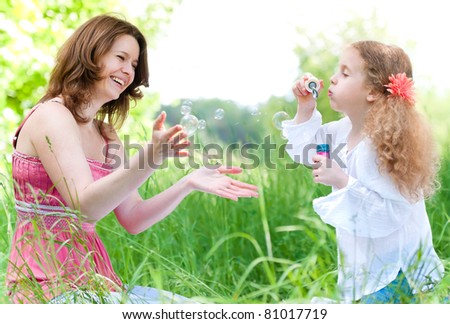 Beautiful young mother together with her daughter in nature making soap bubbles and laughing