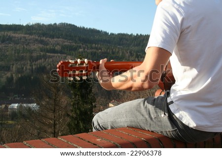 Young man is playing outside, on the roof. Mountain scenery. Mayby he is playing for God and he is worshipping him. He sings.