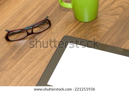 Tablet with blank, white screen and coffee mug and glasses on wooden table.
