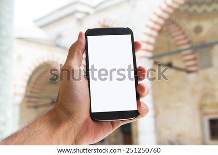 Hand holding smart phone with white blank screen mock up in mosque.