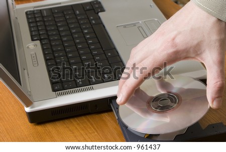 Mans hand placing a cd onto the tray of a laptop
