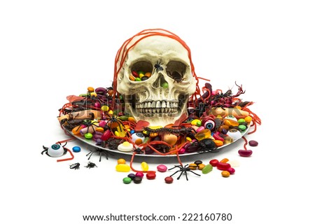 A candy dish filled with trick or treat candy, plastic bug toys and skull on white