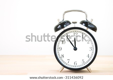 Vintage alarm clock on old wood wall table. /Alarm clock with 5 min before 12 o`clock on old wood table.
