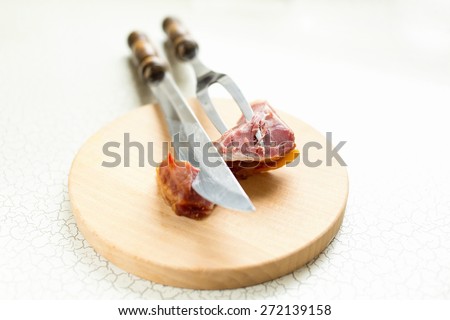 Fork and a large knife for cutting meat or ham are on the cutting boar. Cutting ham or smoked meat.