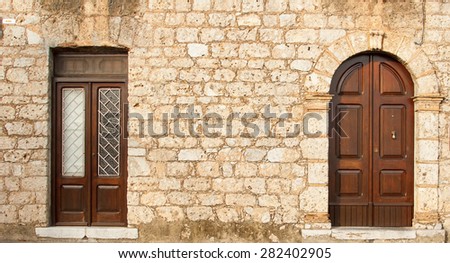 Stone wall with two doors. The wall of an old house in Europe with the front door. Background texture of large stone bricks. Ancient wooden door in stone castle wall. Southern Italy. Europe.