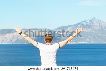 Man traveler looks at the sea and the mountains. Man welcomes nature raised their hands. The traveler enjoys life. Delight.