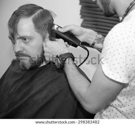 Men\'s hairstyling and haircutting with hair clipper in a barber shop or hair salon. Bearded brutal man in a barber shop. black and white image