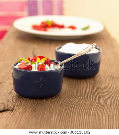 Milk fruit dessert. Whipped cream with strawberries. Serving tasty treats from dairy cream and red strawberries standing on the wooden table. Blue cup with cream and a silver spoon. Berries and cream.