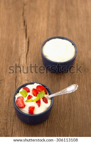 Milk fruit dessert. Whipped cream with strawberries. Serving tasty treats from dairy cream and red strawberries standing on the wooden table. Blue cup with cream and a silver spoon. Berries and cream.