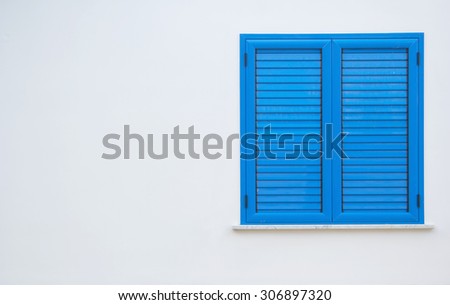 Window with blue shutters on a white wall. Window with closed shutters. Blue window in the wall of the house.