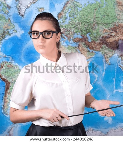 young beautiful woman geography teacher in glasses with black frames with pointer in hand standing in front of world map