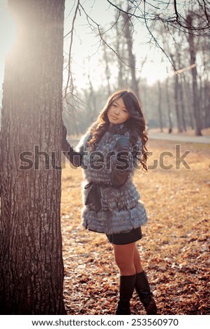 young beautiful asian girl with long hair in a fashionable fur coat walks in autumn park