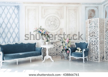 Bright luxury white and blue colored interior living room with flowers in vases. the walls are decorated with baroque ornaments.