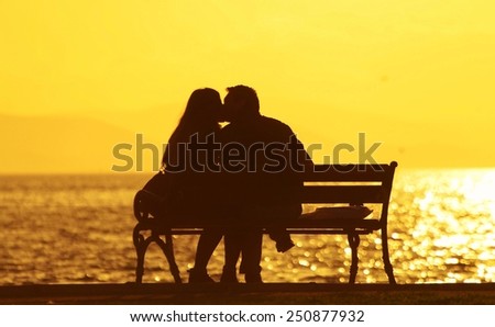 Young couple sitting on a bench under sunset,Young couple kissing on a bench under sunset.