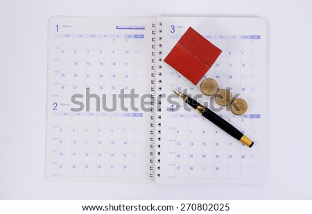 Fountain pen and coins and paper house on calendar book pages for Mortgage loan planning concept