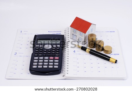 Mortgage loan planning with fountain pen and calculator and coins and paper house on calendar book pages for loans concept