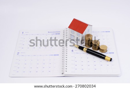 Mortgage loan planning concept with fountain pen and coins and paper house on calendar book pages